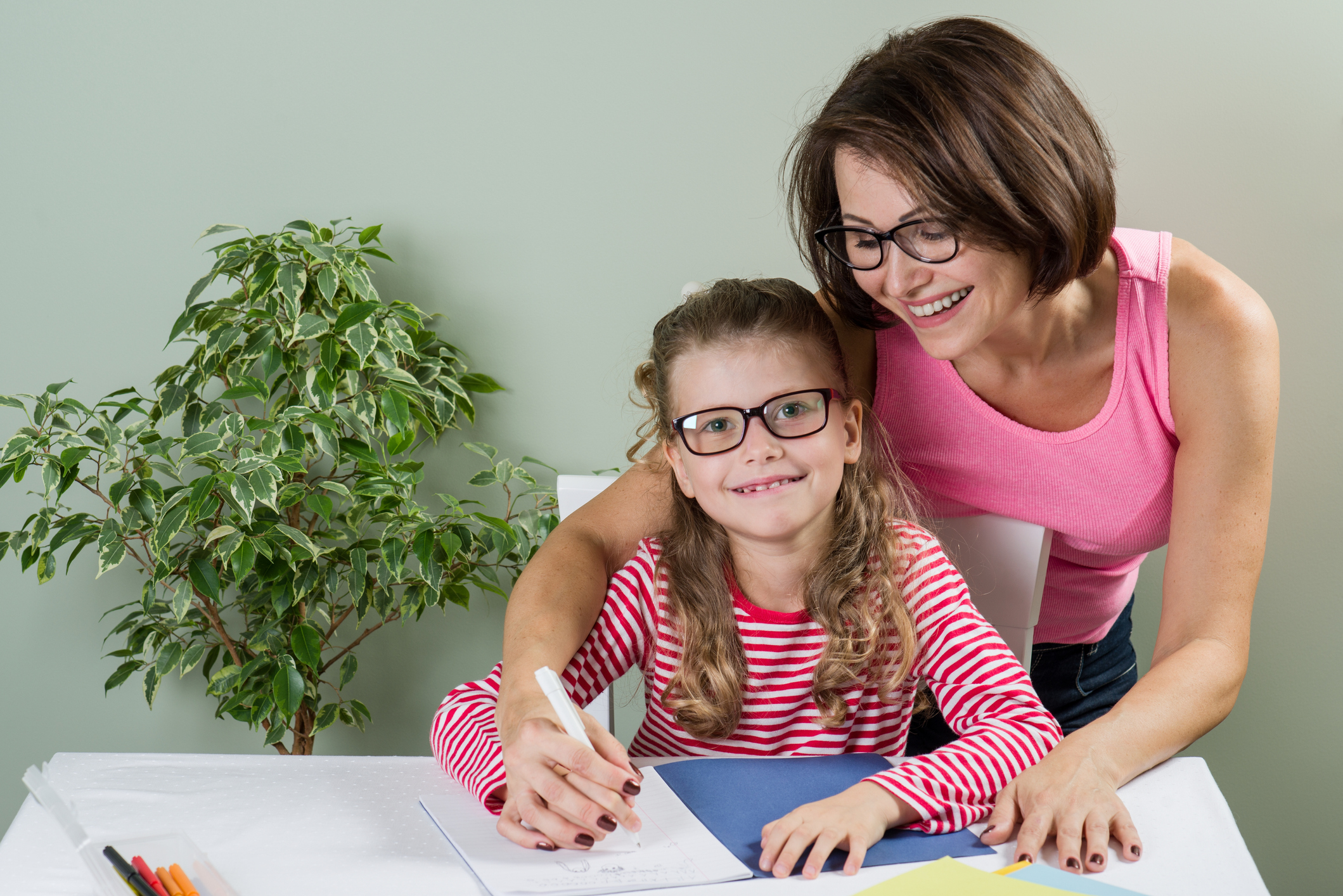 Young girl sitting at desk with woman behind her helping her write